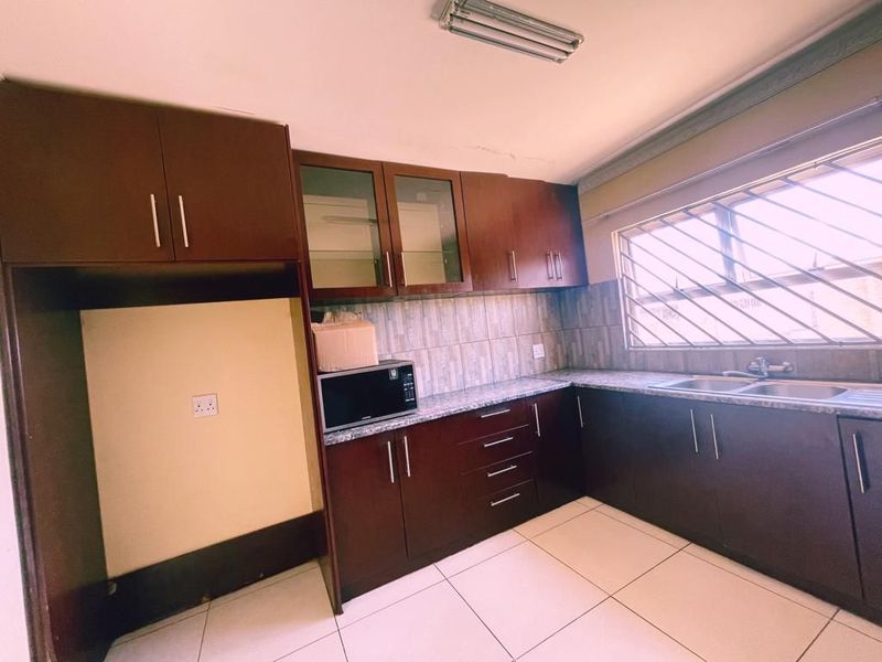 A functional kitchen featuring dark wood cabinetry, granite countertops, a double stainless steel sink, and tiled flooring, offering a practical layout for daily use.