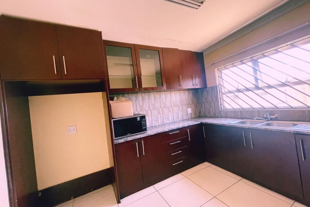 A functional kitchen featuring dark wood cabinetry, granite countertops, a double stainless steel sink, and tiled flooring, offering a practical layout for daily use.