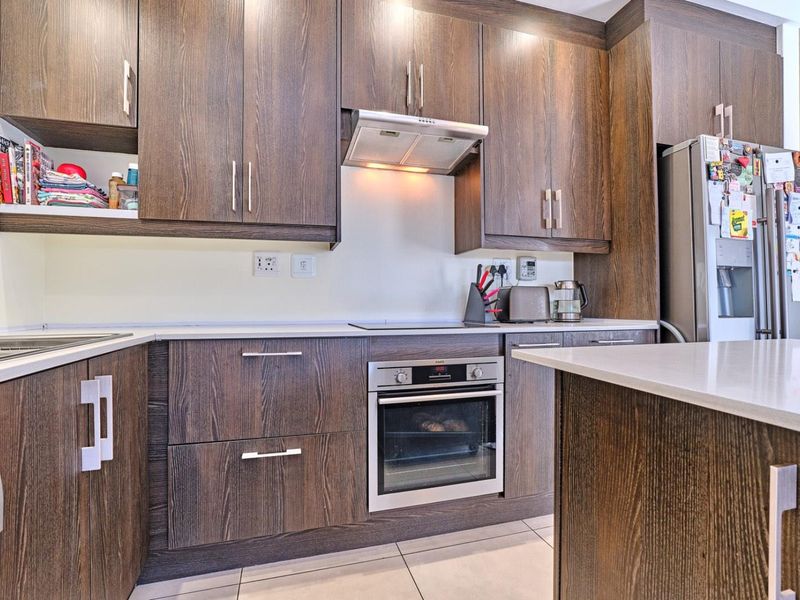 Modern kitchen featuring dark wood-grain cabinetry, stone countertops, integrated oven, hob, and extractor fan with tiled flooring.