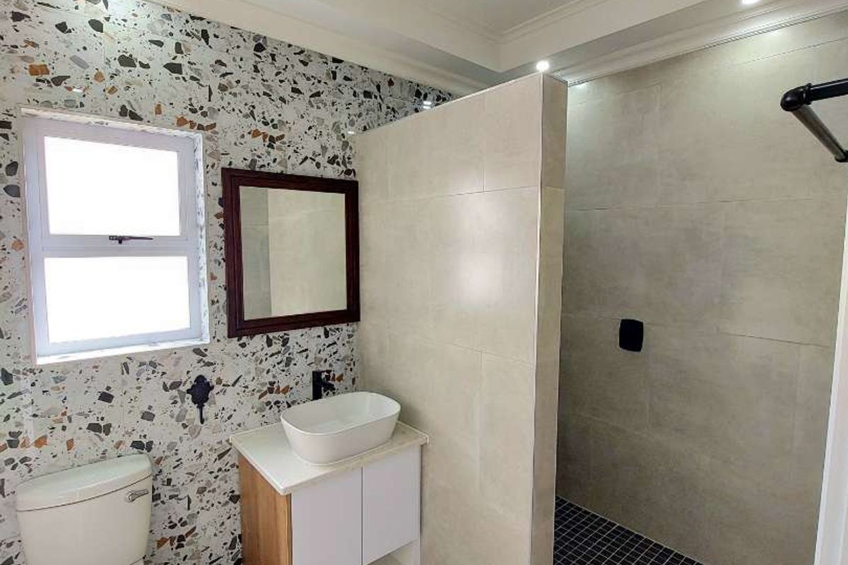 Modern bathroom featuring a walk-in shower with black mosaic tiling, a vessel sink vanity, and a distinctive terrazzo-style feature wall.