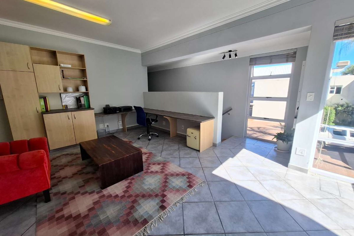 A functional living area featuring tiled flooring, built-in cabinetry, a desk workspace, and natural light from large aluminium windows.