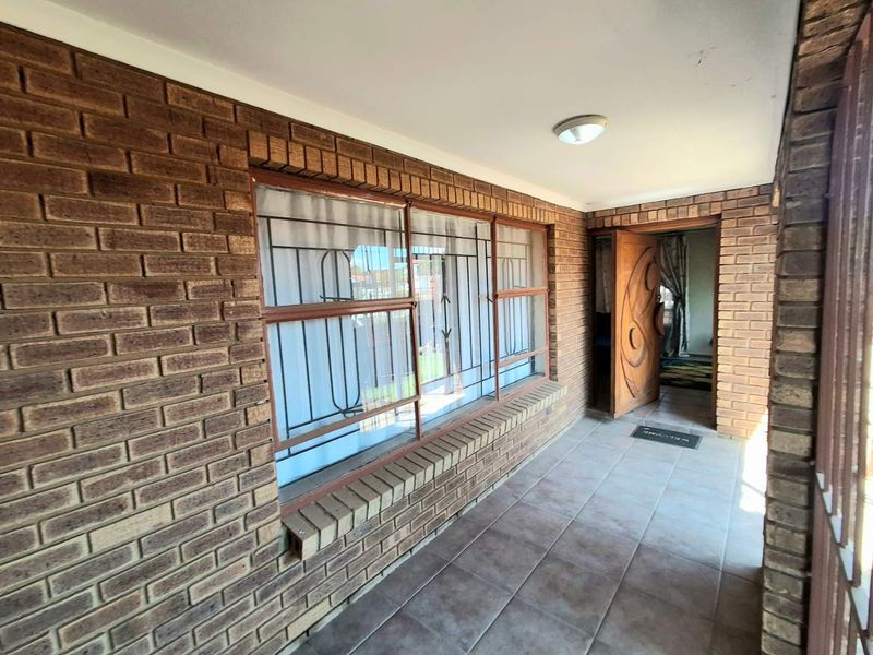 A covered patio area featuring face brick walls, tiled flooring, and a solid wood entrance door with security bars on the windows.