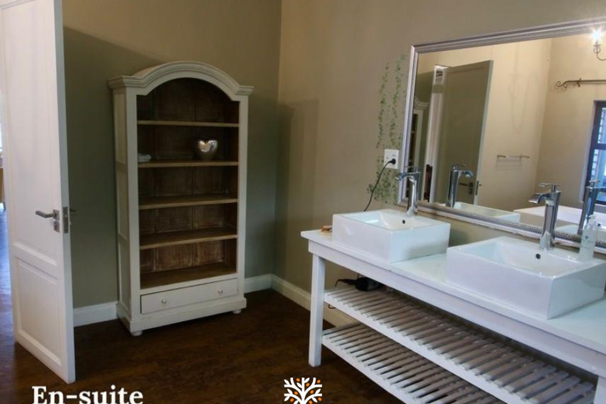 A modern en-suite bathroom featuring a double vanity with vessel sinks, chrome faucets, and a large wall-mounted mirror.