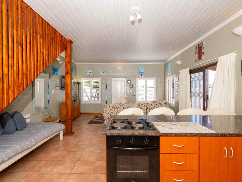Open-plan living area featuring a kitchen with granite countertops, built-in oven and hob, tiled flooring, and a timber staircase leading to the upper level.