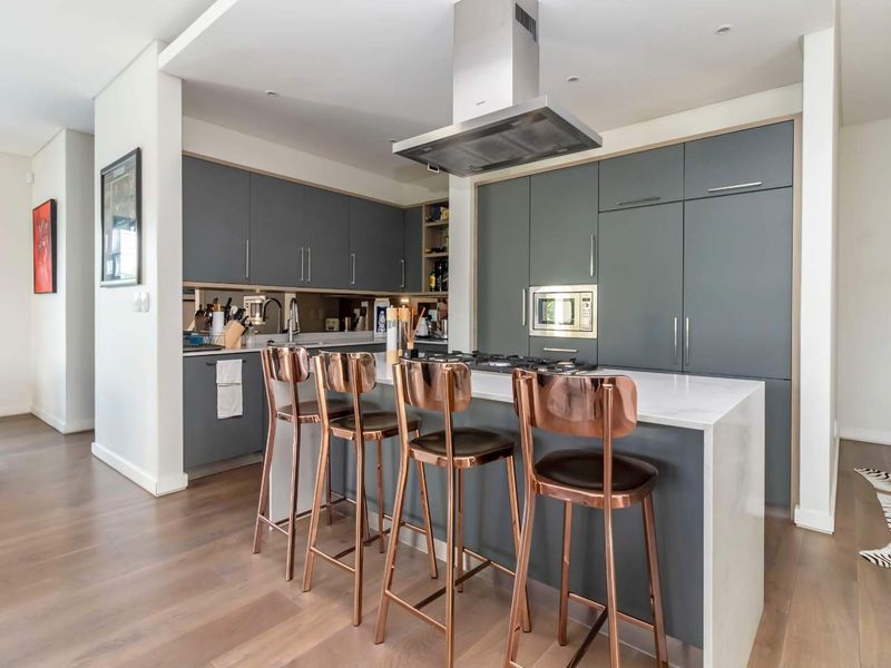 Modern kitchen featuring sleek grey cabinetry, a central island with stone countertop, integrated appliances, and a stylish mirrored backsplash.