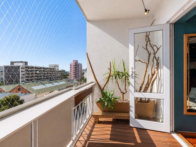 A well-maintained balcony featuring timber decking, a metal balustrade, and safety netting, offering an open-air space with urban views.