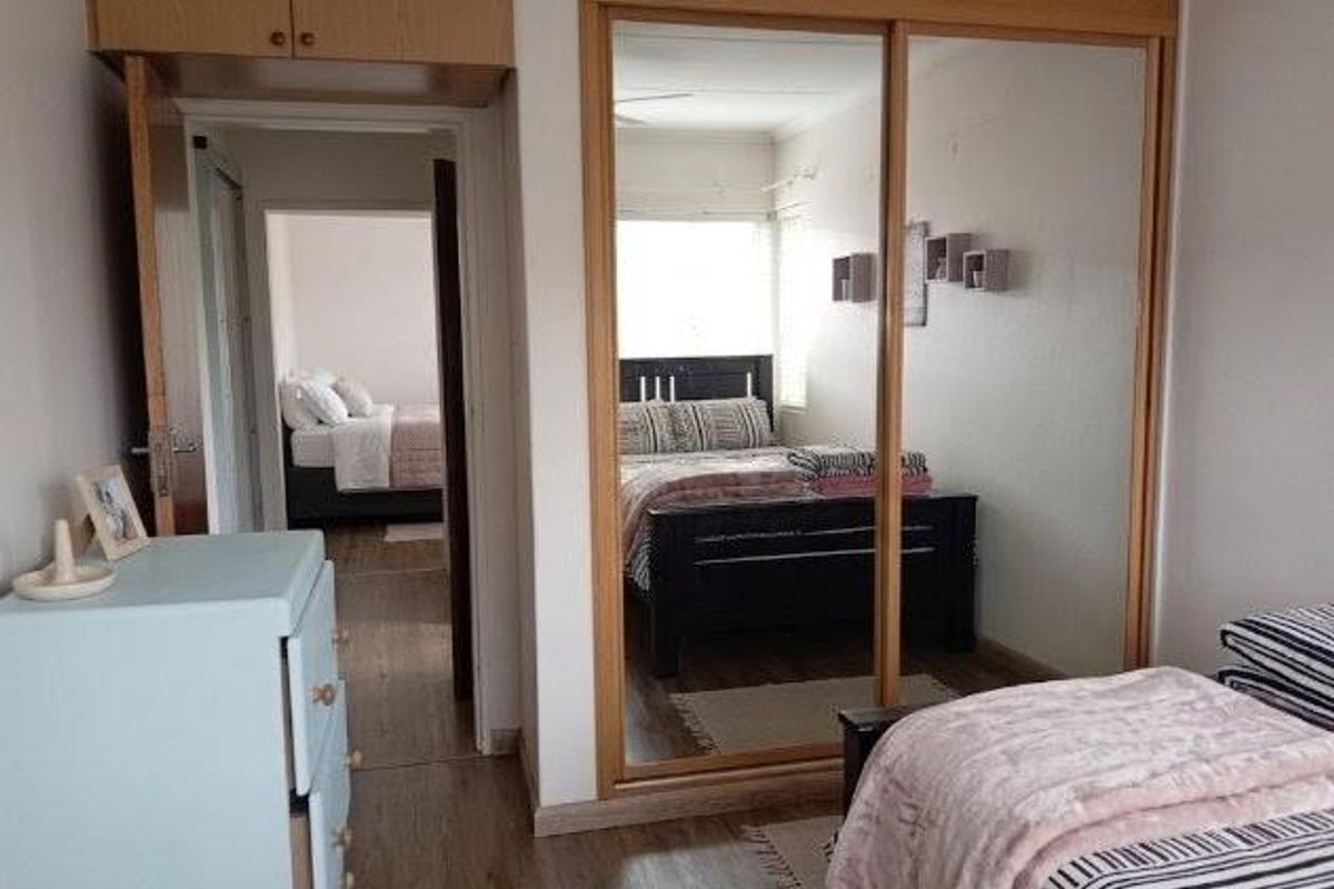 Bedroom featuring built-in cupboards with mirrored sliding doors, overhead storage cabinetry, and laminate flooring, with a view into an adjacent bedroom.