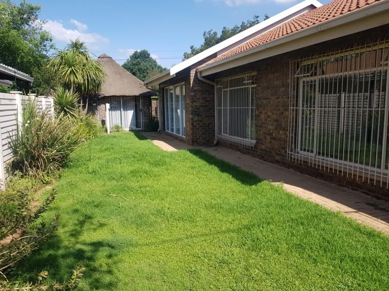 Rear view of the property featuring a face brick facade, tiled roof, security bars on windows, a paved walkway, and a separate thatched lapa.