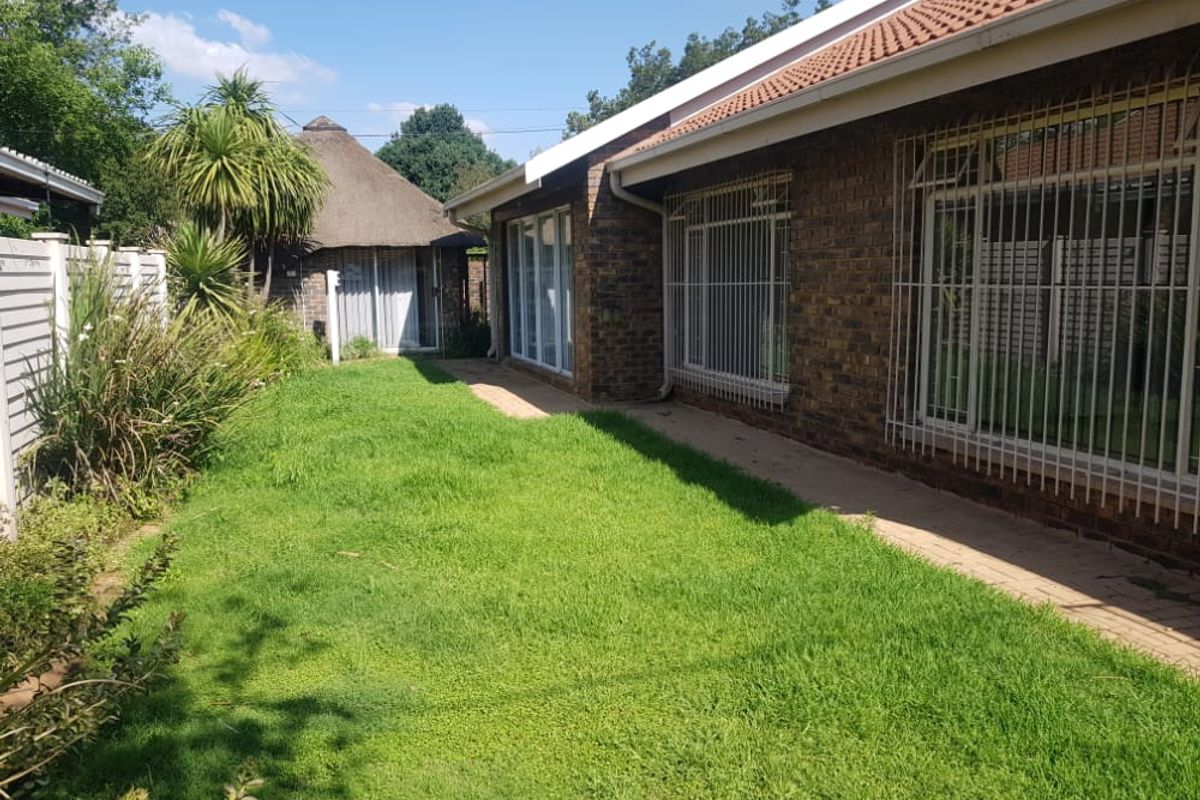 Rear view of the property featuring a face brick facade, tiled roof, security bars on windows, a paved walkway, and a separate thatched lapa.
