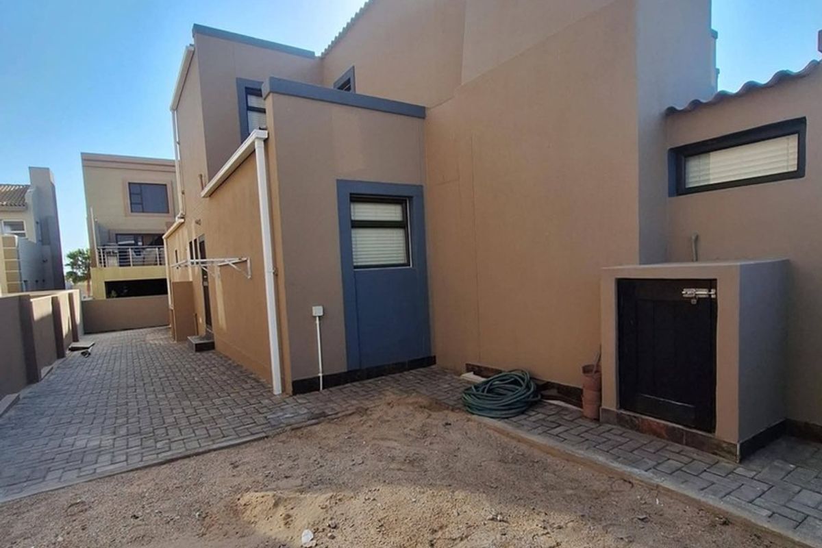 Rear exterior view of the property featuring paved walkways, a built-in storage unit, and an unlandscaped garden area ready for development.