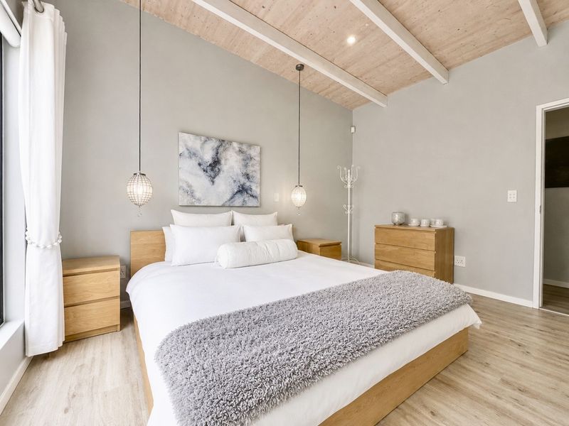 A well-maintained bedroom featuring light wood laminate flooring, exposed timber ceiling beams, and modern pendant lighting, creating a bright and inviting atmosphere.