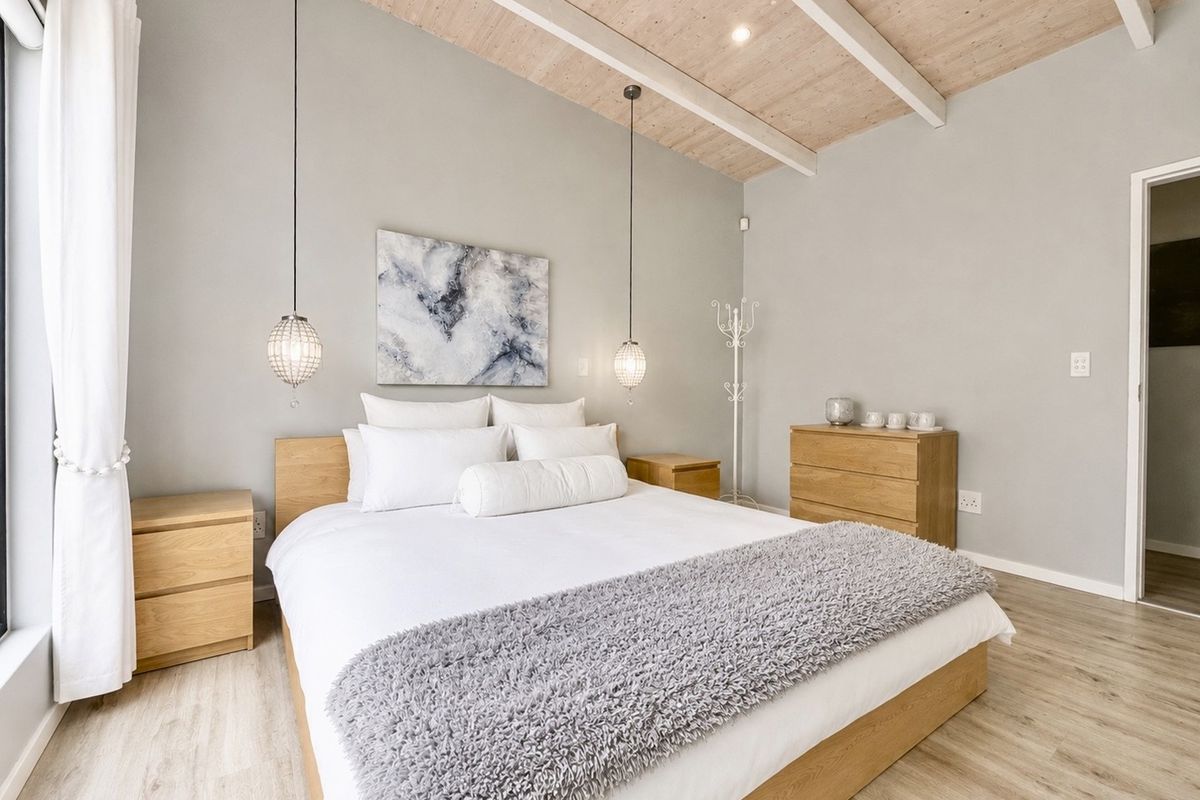 A well-maintained bedroom featuring light wood laminate flooring, exposed timber ceiling beams, and modern pendant lighting, creating a bright and inviting atmosphere.