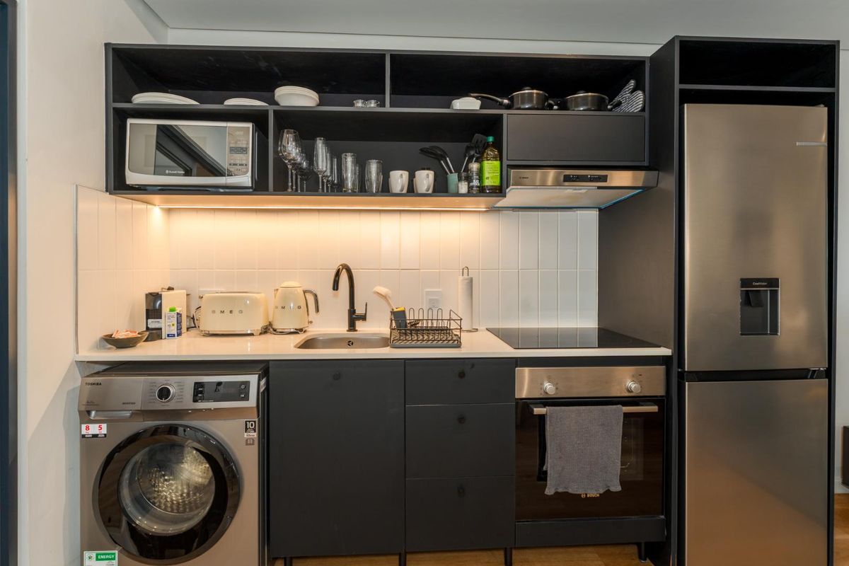 Modern compact kitchen featuring dark cabinetry, subway tile backsplash, integrated appliances, and efficient under-cabinet lighting.
