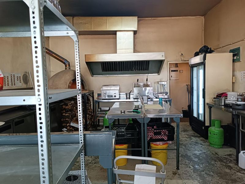 Commercial kitchen space featuring a wood-fired pizza oven, stainless steel prep stations, commercial extraction hood, and industrial refrigeration units.