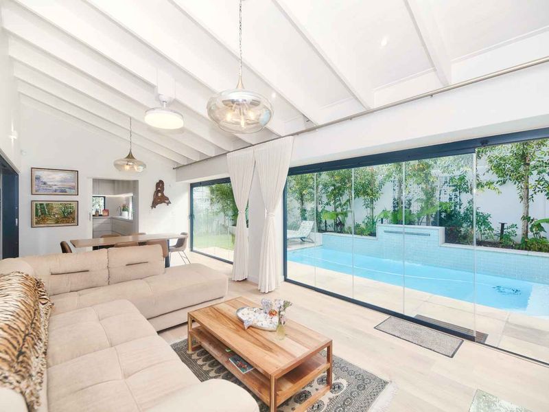 Bright open-plan living area featuring vaulted ceilings with exposed beams, hardwood floors, and seamless indoor-outdoor flow to a private swimming pool and garden.