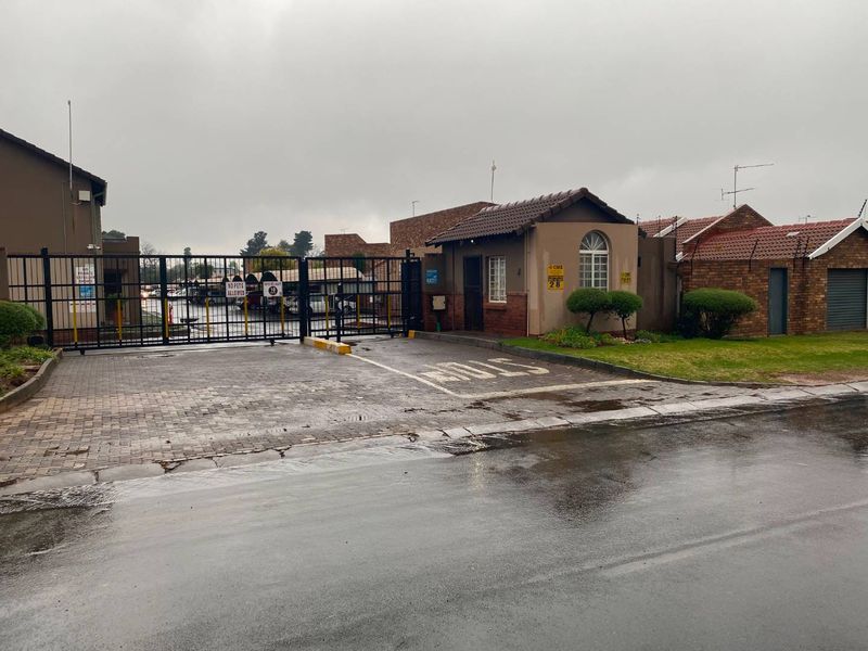 Front entrance view of the apartment complex featuring a secure gated access point, guard house, and paved driveway.