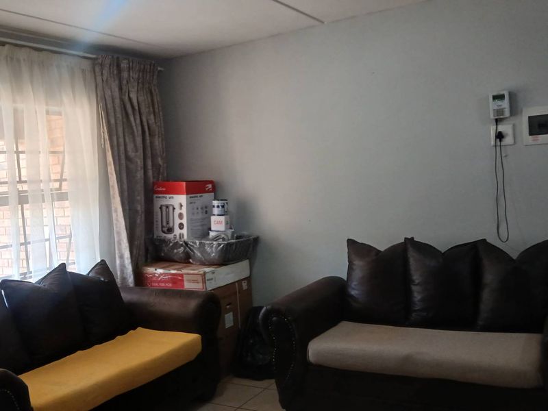 A living room area featuring tiled flooring, a security alarm keypad, and an electrical distribution board mounted on the wall.