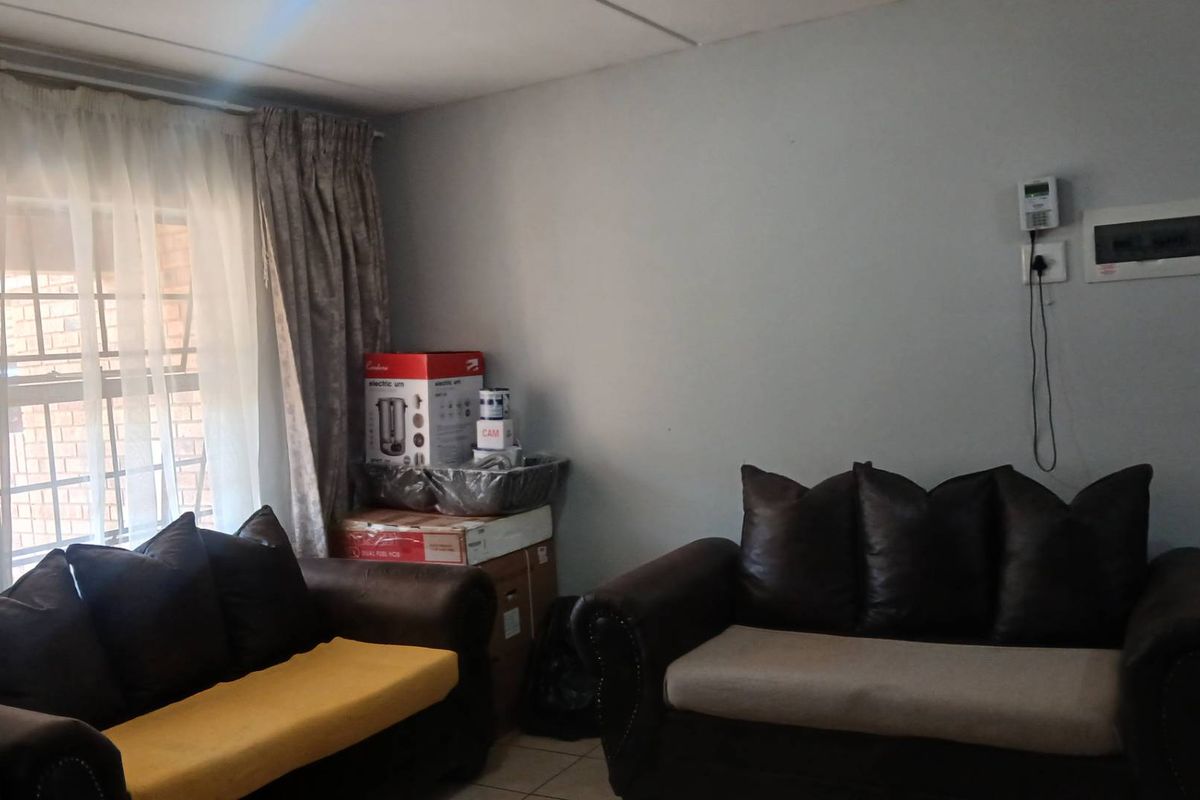 A living room area featuring tiled flooring, a security alarm keypad, and an electrical distribution board mounted on the wall.