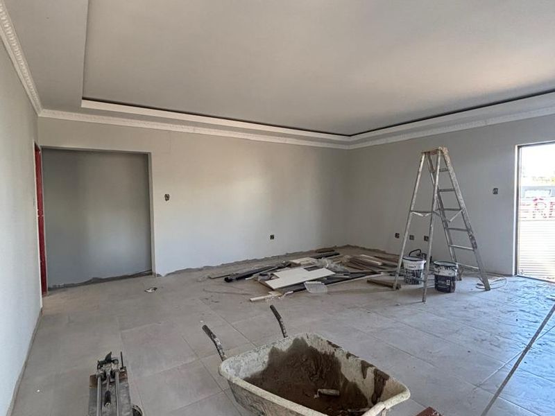 An unfinished living room space featuring tiled flooring and a recessed ceiling with decorative coving, currently undergoing renovation.