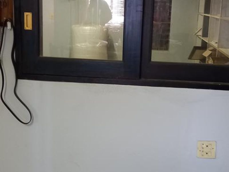 An interior office space featuring a dark-framed sliding window, tiled flooring, and basic electrical infrastructure, suitable for a functional workspace.