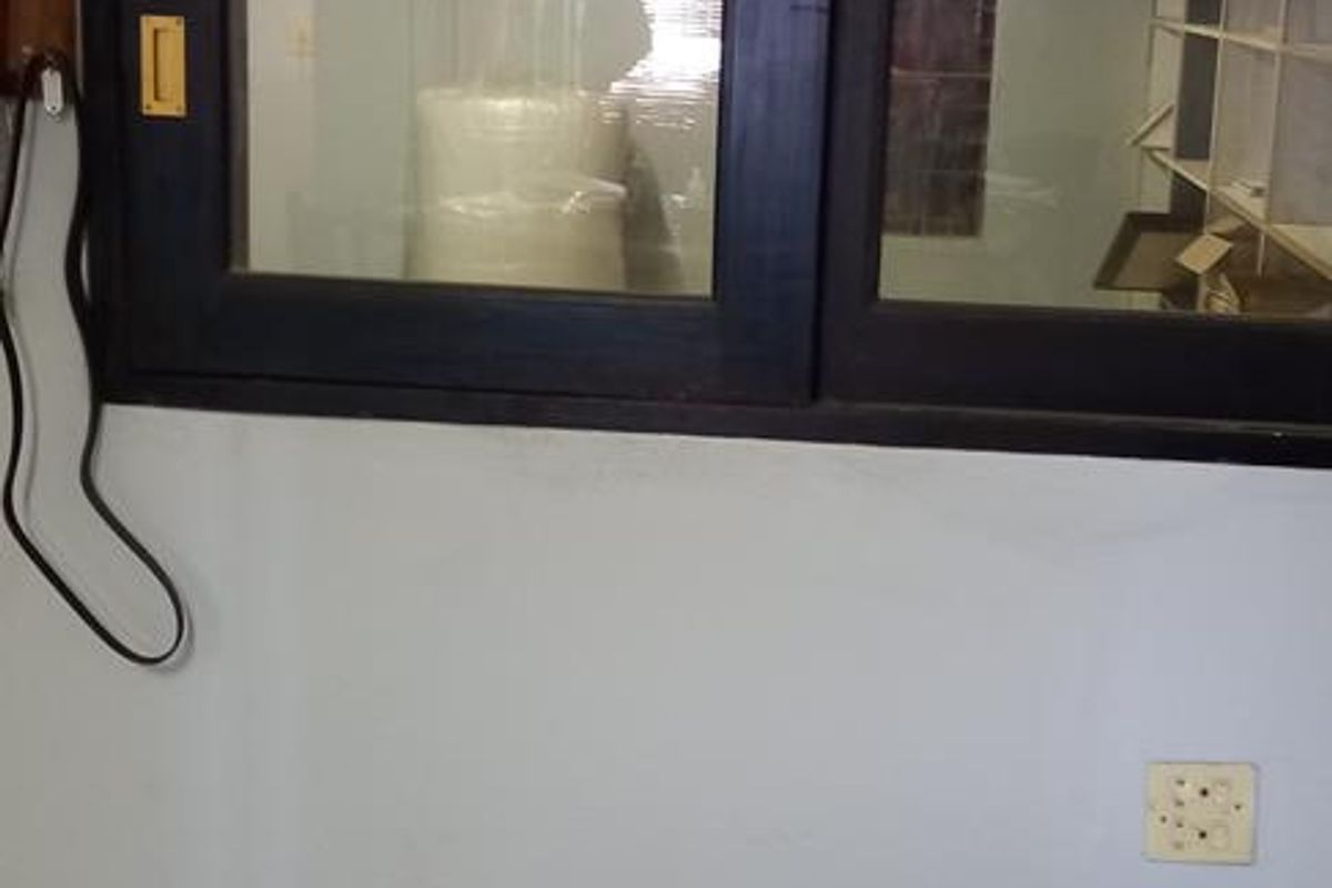 An interior office space featuring a dark-framed sliding window, tiled flooring, and basic electrical infrastructure, suitable for a functional workspace.
