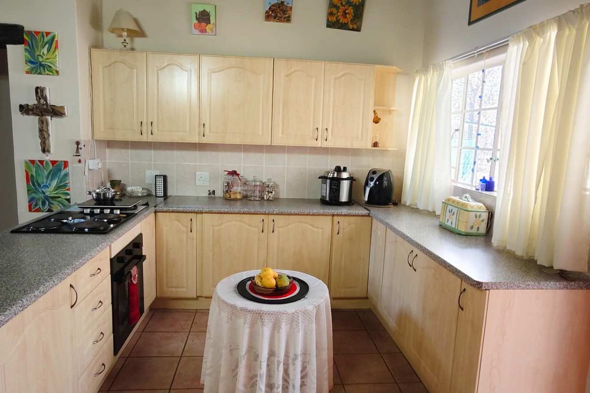 A functional kitchen featuring light wood cabinetry, granite-style countertops, a built-in oven, and a gas hob, with tiled flooring throughout.