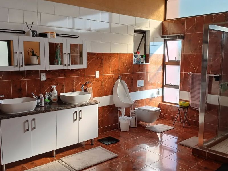 Spacious bathroom featuring a double vanity with vessel sinks, a wall-mounted toilet, a urinal, and a glass-enclosed shower with decorative tiled finishes.