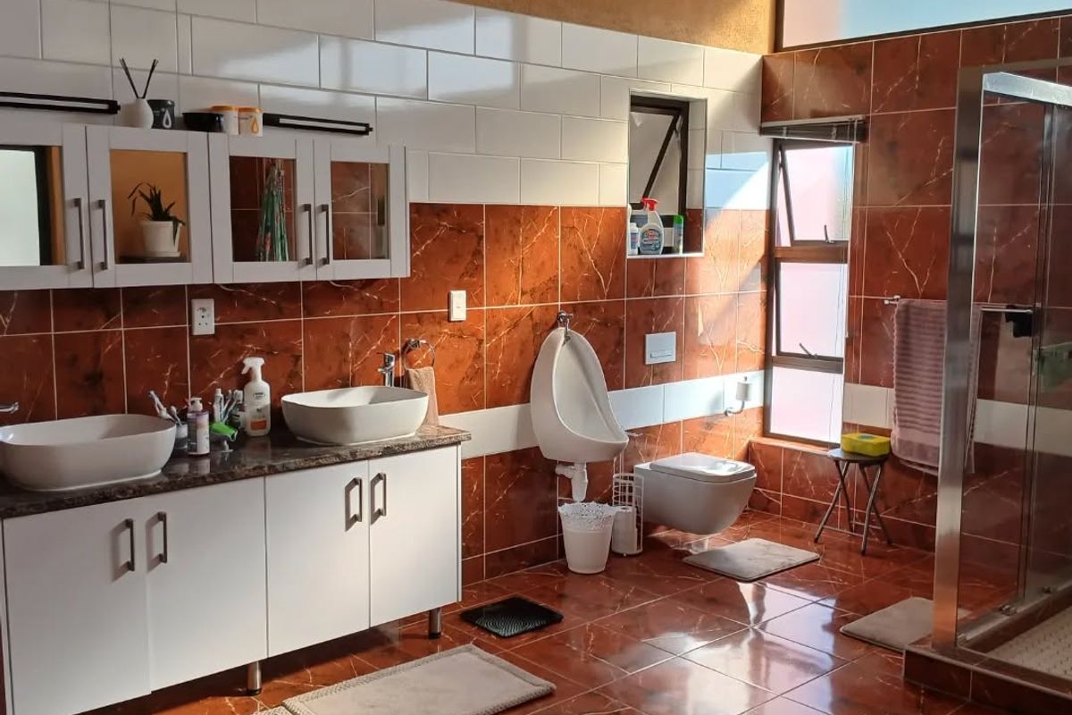 Spacious bathroom featuring a double vanity with vessel sinks, a wall-mounted toilet, a urinal, and a glass-enclosed shower with decorative tiled finishes.