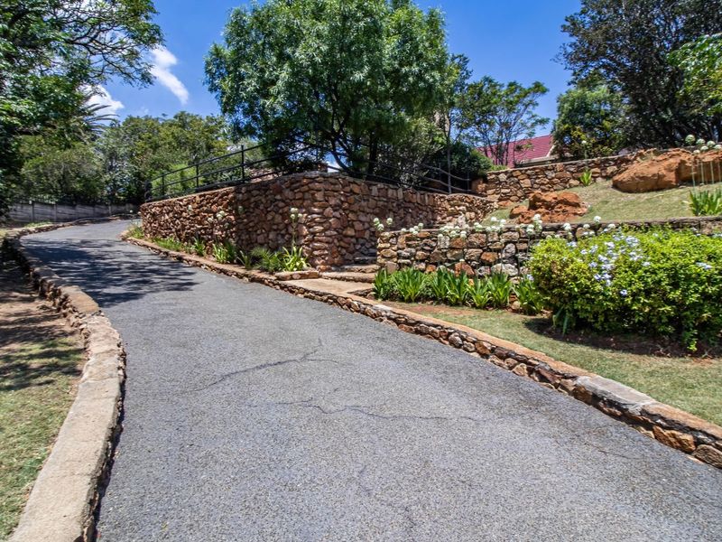 A paved driveway leading up to the property, featuring tiered stone retaining walls and established garden landscaping.