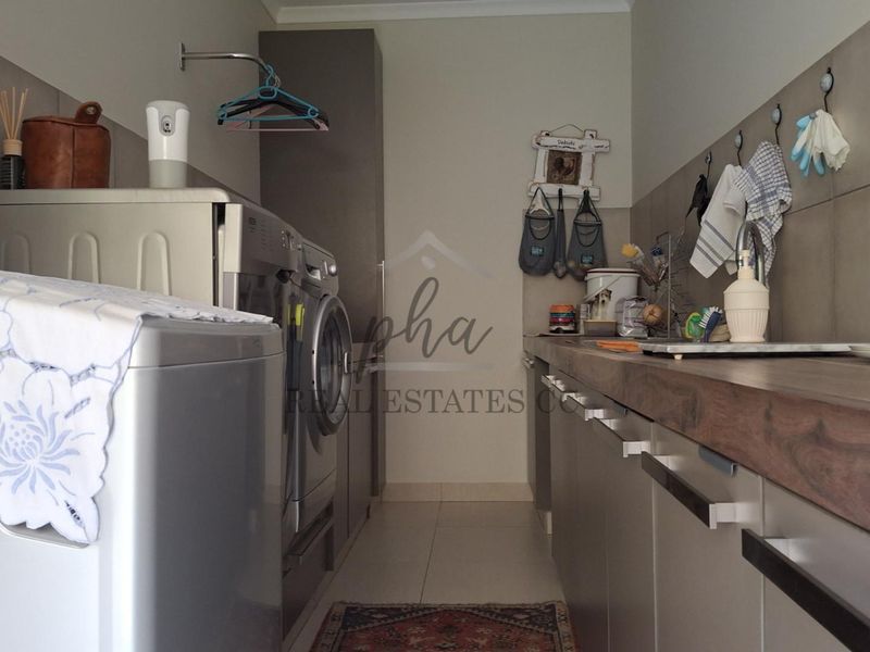 Functional laundry room featuring built-in cabinetry, a timber countertop, and tiled splashback, providing efficient space for washing and utility tasks.