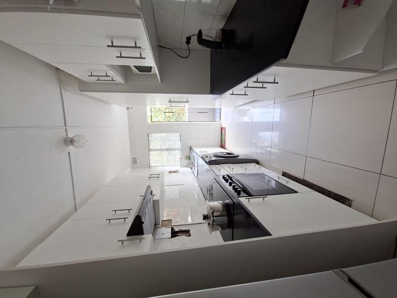 A galley-style kitchen featuring white cabinetry, black countertops, built-in oven, and hob, with tiled flooring and backsplash.