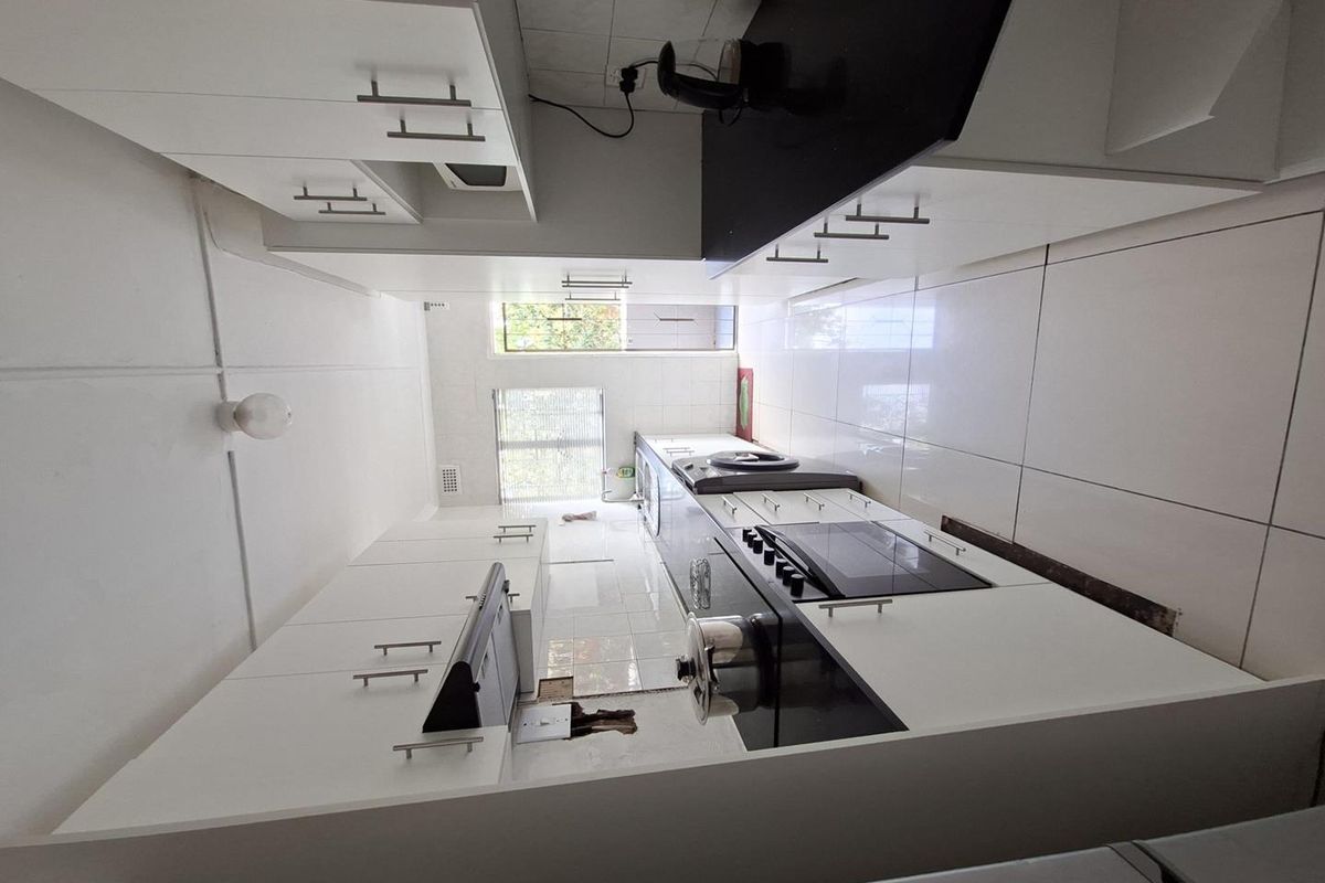 A galley-style kitchen featuring white cabinetry, black countertops, built-in oven, and hob, with tiled flooring and backsplash.