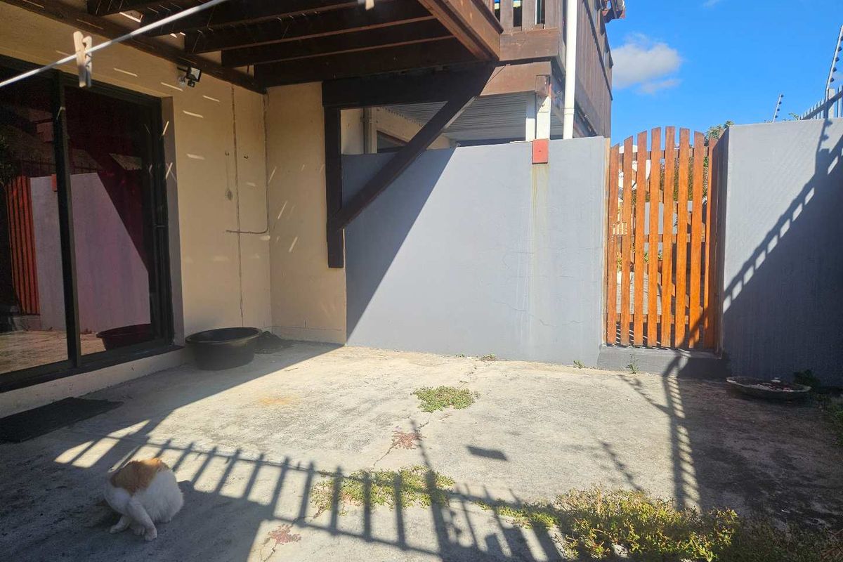 A private rear courtyard area featuring concrete paving, a timber gate, and a covered patio section attached to the main building structure.