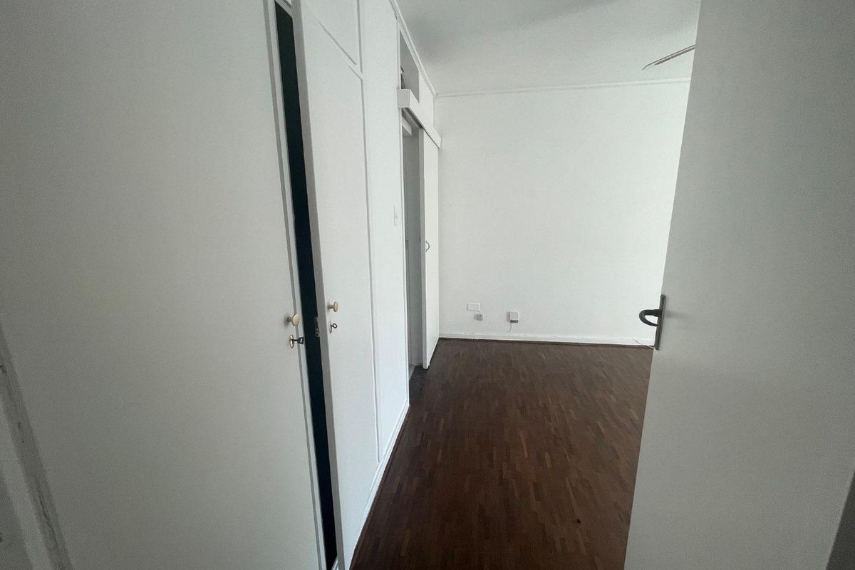 An empty bedroom featuring dark parquet flooring and extensive built-in cupboard storage with white cabinetry.