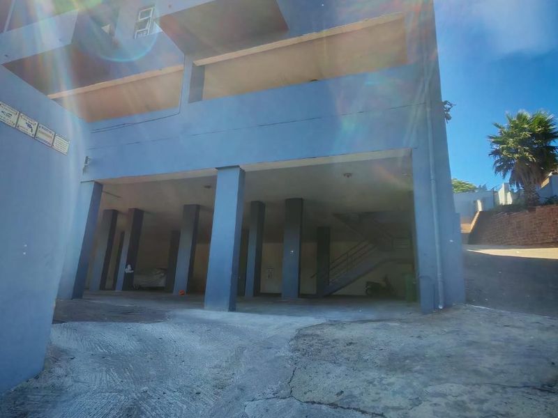 Front elevation of an apartment building featuring a covered ground-level parking area, concrete pillars, and external stairwell access.