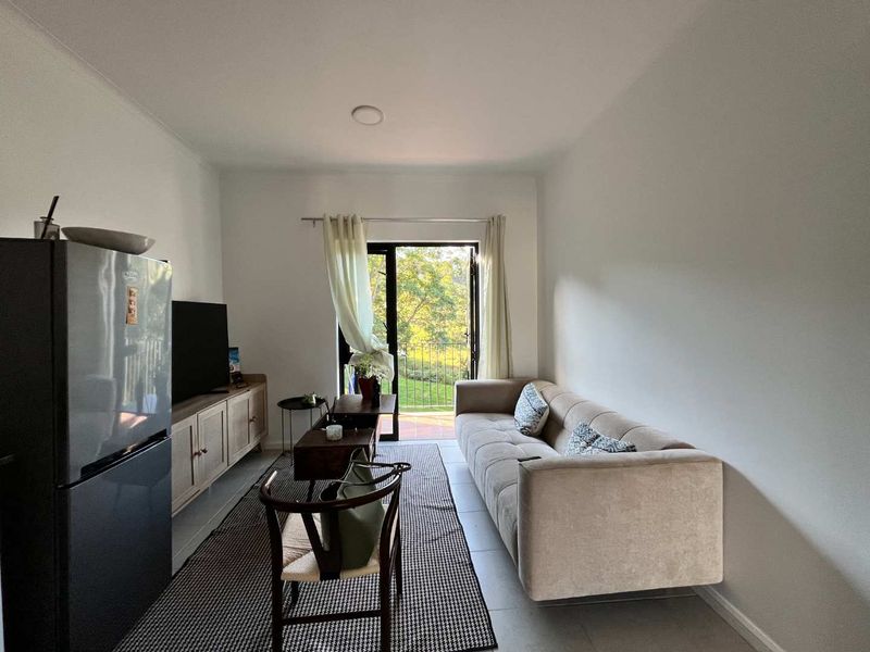 A bright living room featuring tiled flooring and a glass door providing direct access to a balcony with scenic outdoor views.