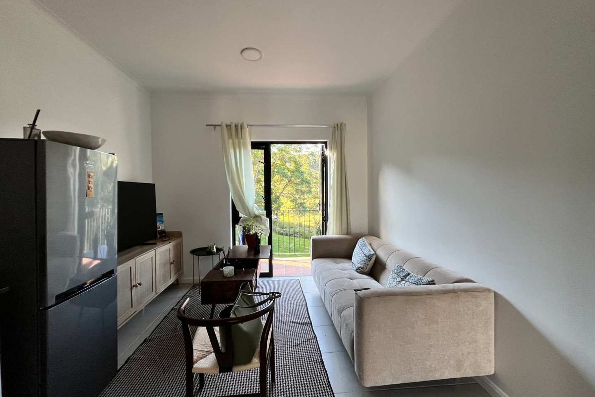 A bright living room featuring tiled flooring and a glass door providing direct access to a balcony with scenic outdoor views.