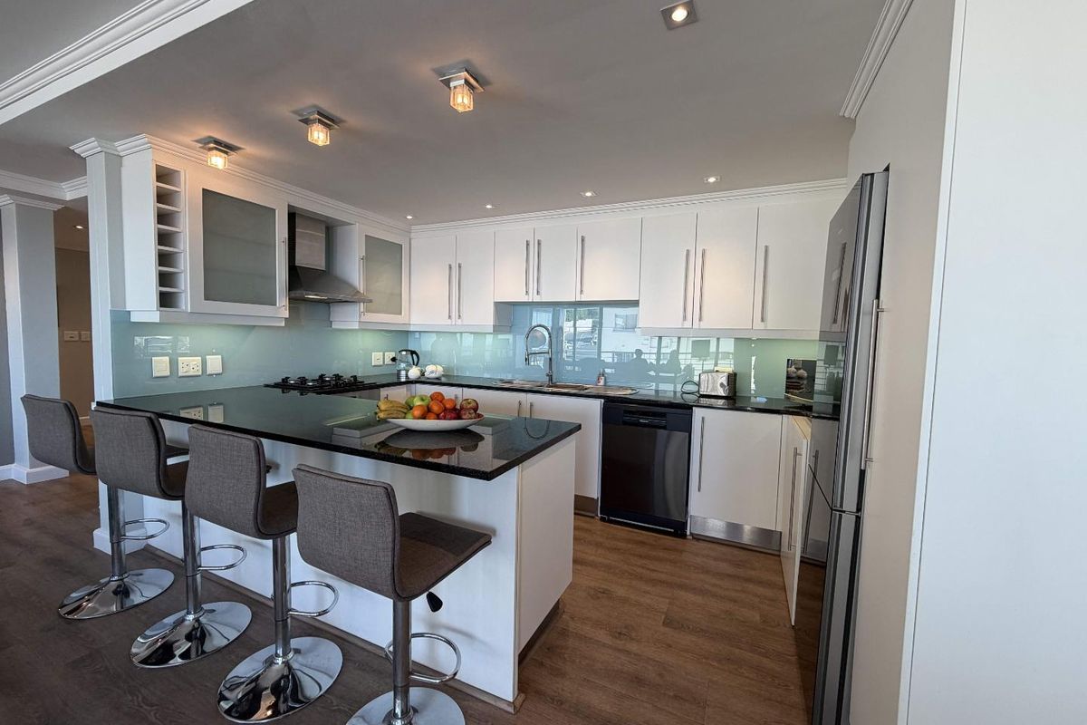 Modern kitchen featuring white cabinetry, granite countertops, glass splashback, integrated appliances, and a breakfast bar with recessed lighting.