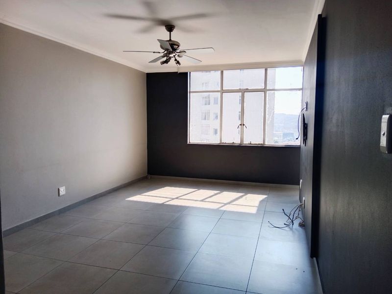 An empty living room featuring large windows, tiled flooring, and a ceiling fan, offering a blank canvas for personalization.