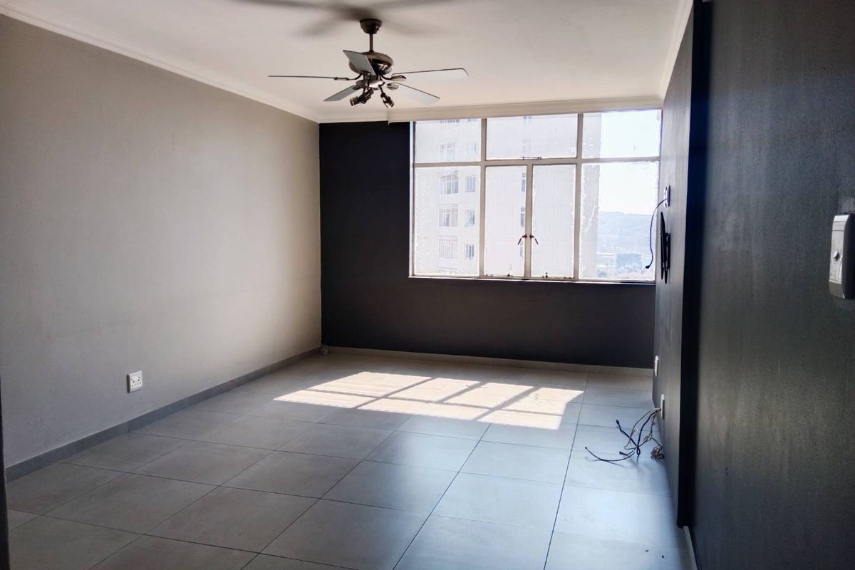An empty living room featuring large windows, tiled flooring, and a ceiling fan, offering a blank canvas for personalization.