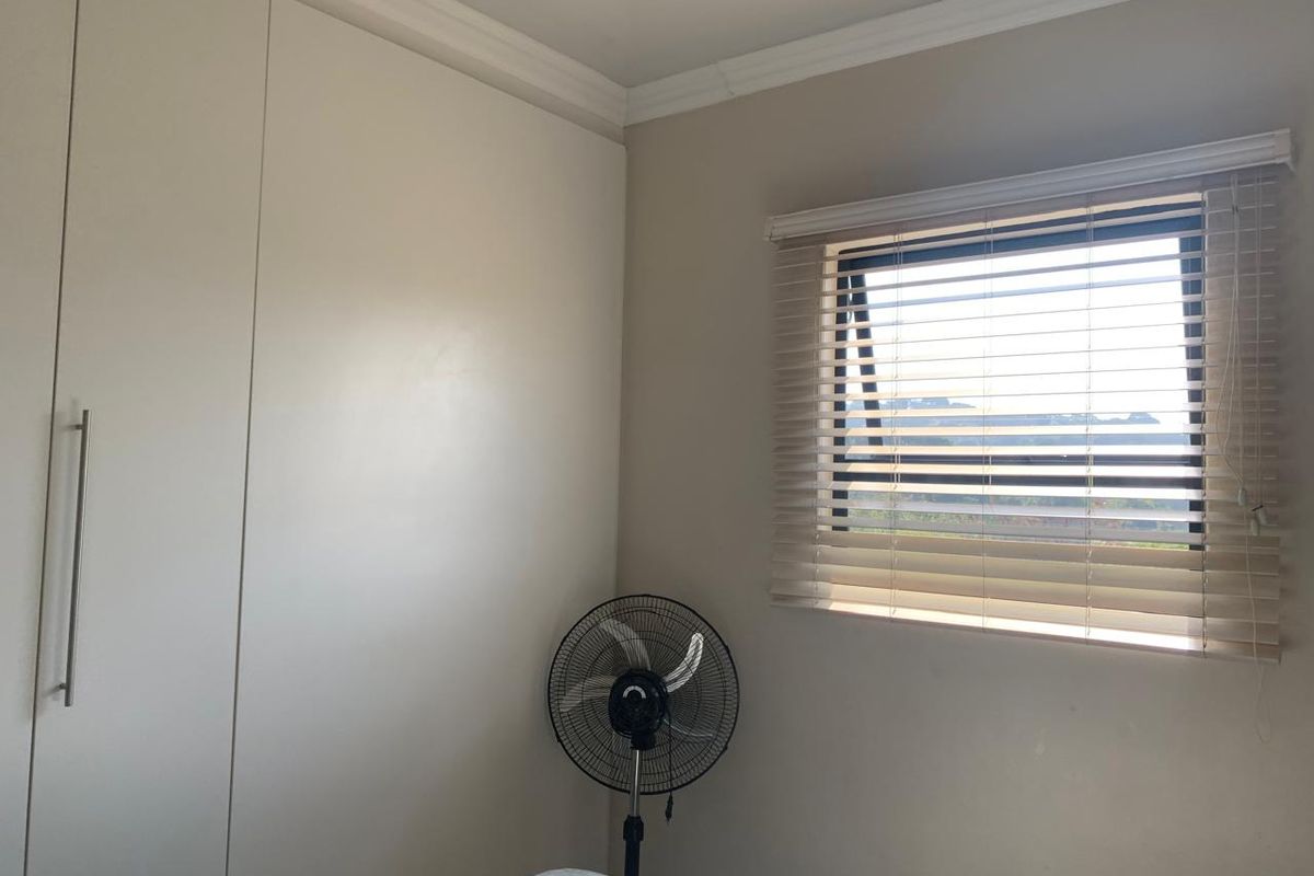 A bedroom featuring neutral walls, built-in cupboards, and a top-hung window fitted with venetian blinds.
