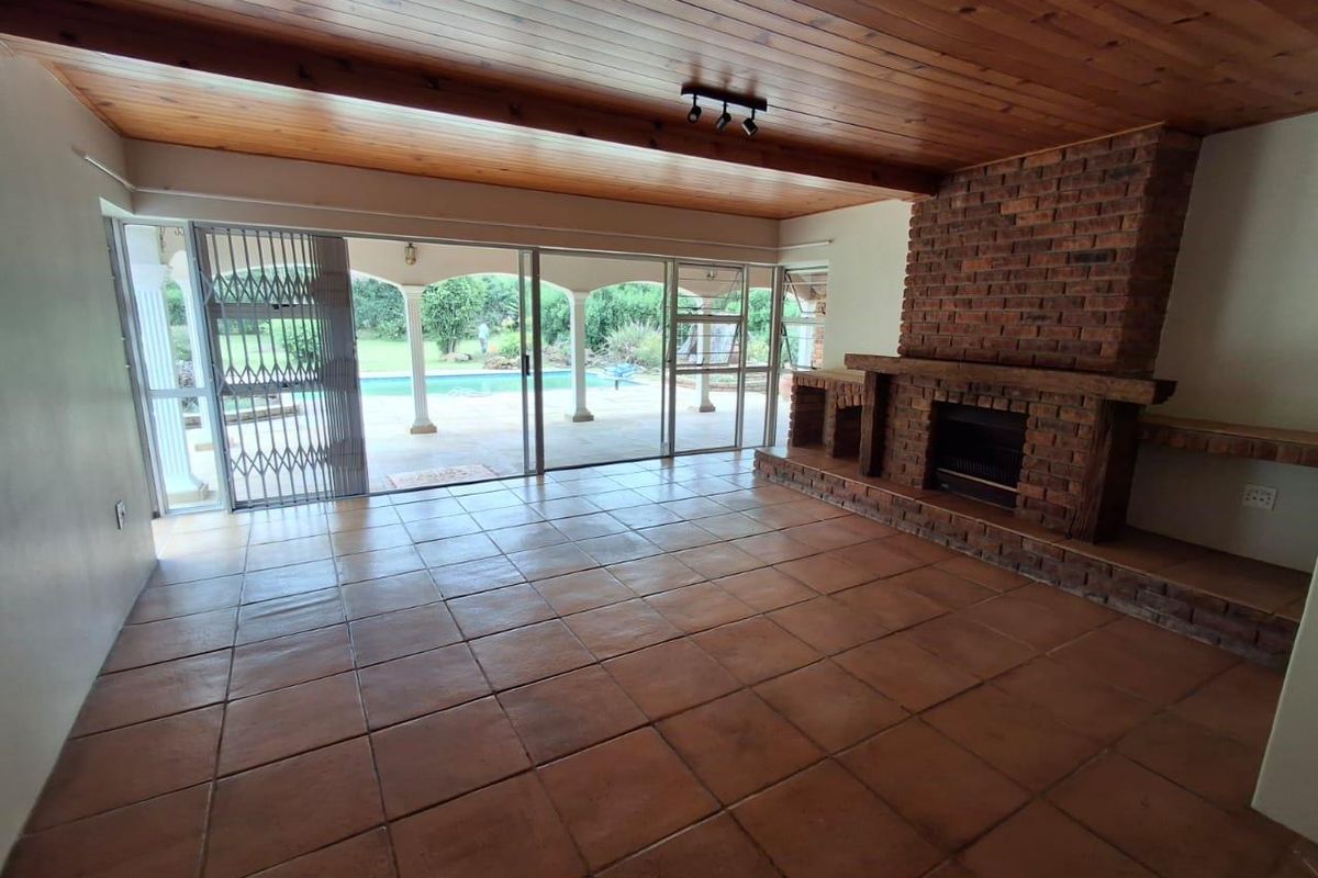 Spacious living room featuring a large brick fireplace, timber-clad ceiling, and sliding glass doors opening onto a covered patio and pool area.