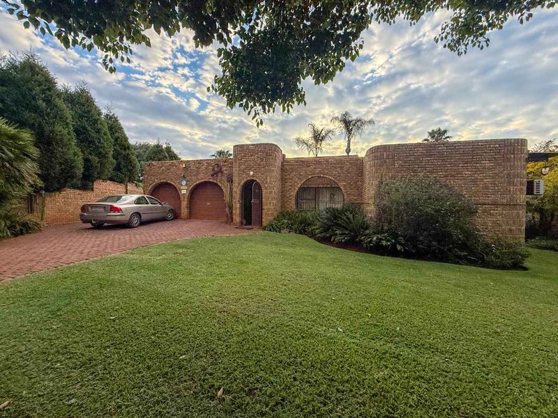 Front elevation of a face brick house featuring arched architectural details, a paved driveway, and a well-maintained front lawn.