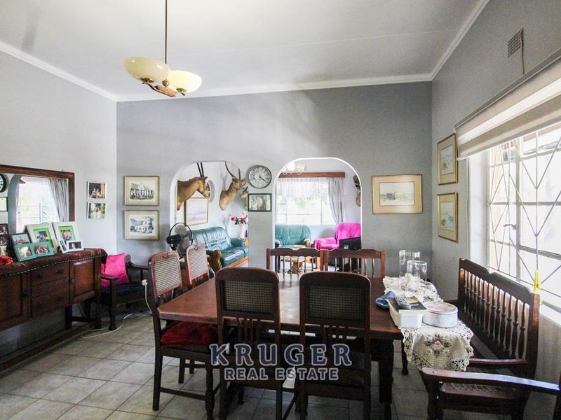 A spacious dining room featuring tiled flooring, classic archways leading to an adjacent living area, and large steel-framed windows providing natural light.