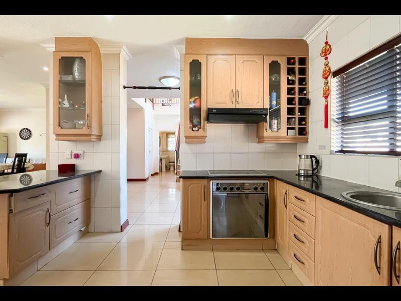 A functional kitchen featuring light wood cabinetry, granite countertops, built-in oven and hob, and tiled finishes, offering a practical layout for daily cooking.