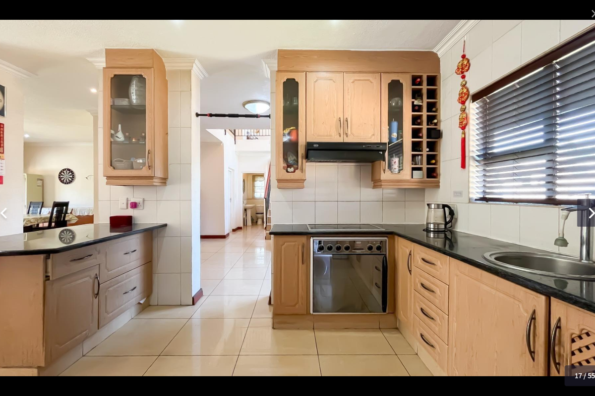 A functional kitchen featuring light wood cabinetry, granite countertops, built-in oven and hob, and tiled finishes, offering a practical layout for daily cooking.