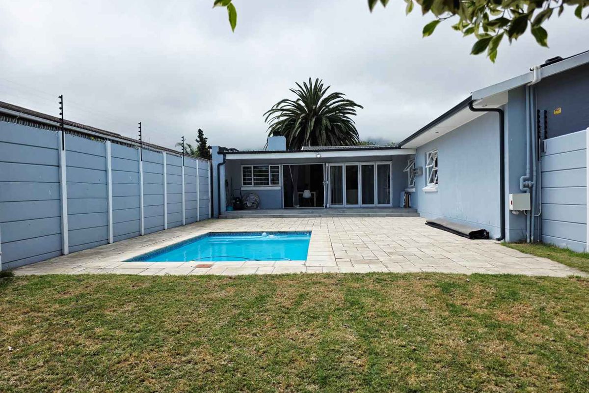Rear exterior view featuring a swimming pool, paved patio area, and enclosed garden space with perimeter walling.