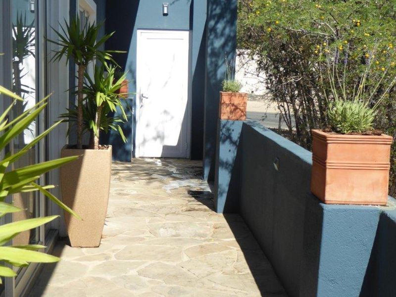 A paved outdoor patio area featuring stone flooring, a sliding glass door entrance, and a painted masonry boundary wall.