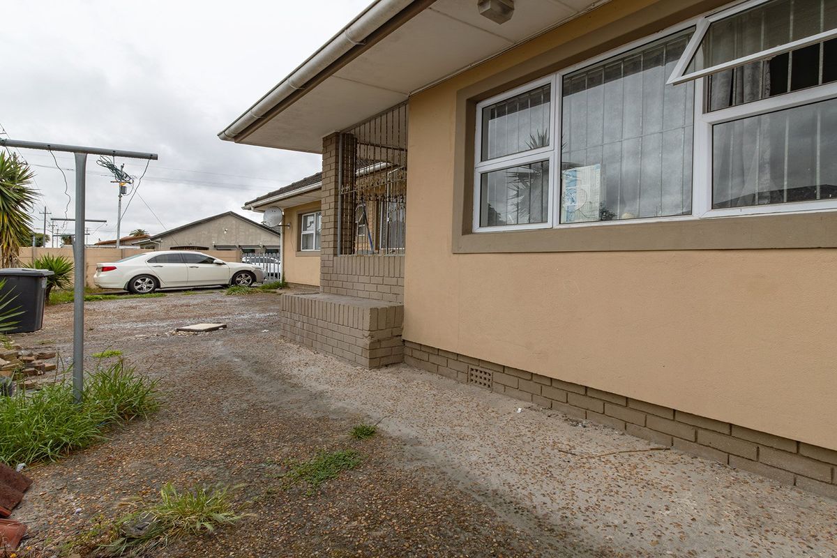 Rear exterior view of the house featuring a concrete apron, security bars on windows, and a brick plinth foundation.