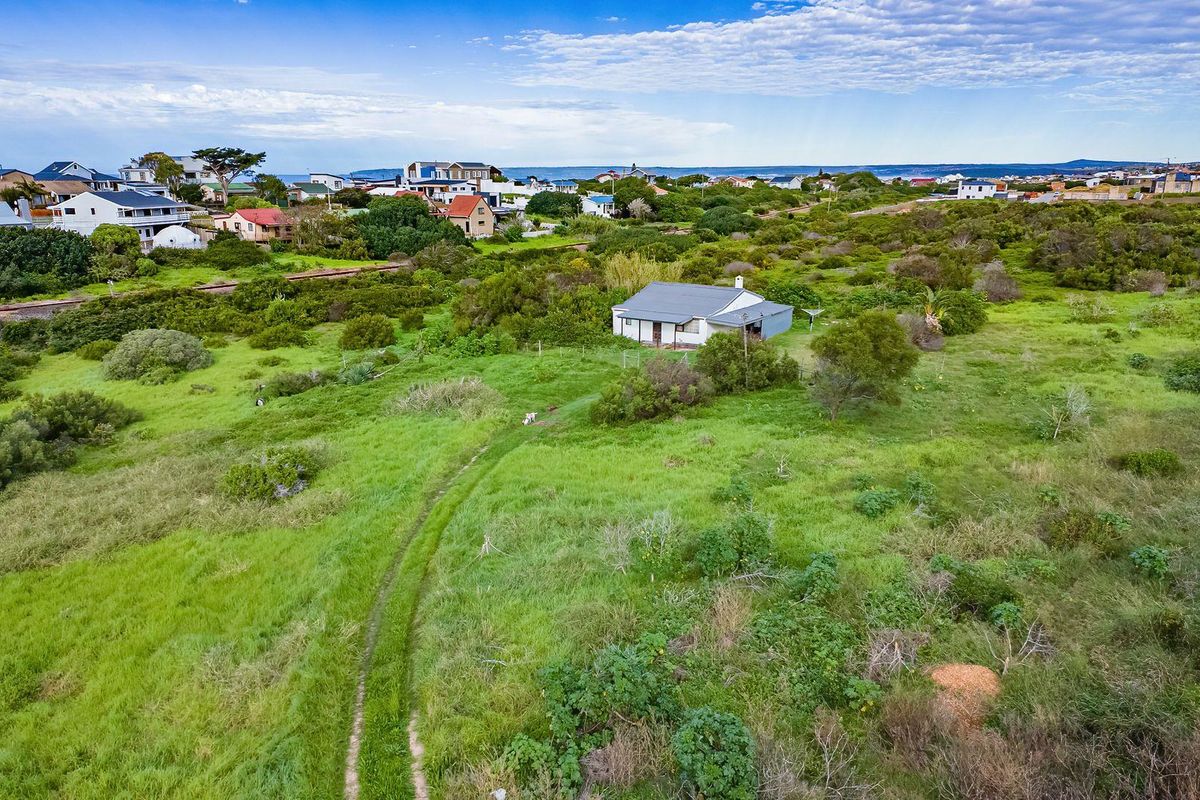 Aerial view of a residential plot featuring a small dwelling surrounded by natural vegetation and established neighborhood surroundings.